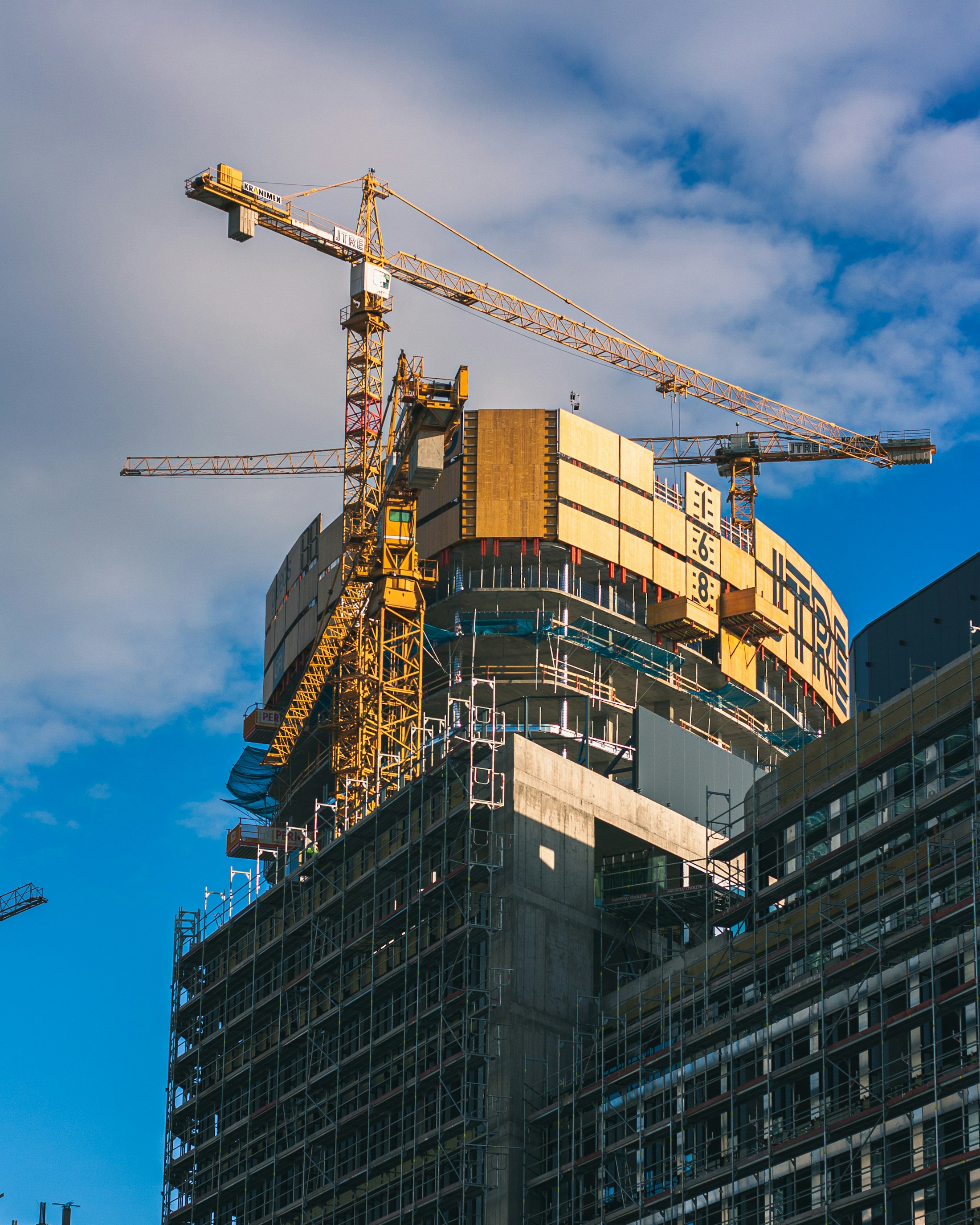 Tower crane di sisi gedung tinggi yang sedang dibangun; foto ilustrasi konstruksi